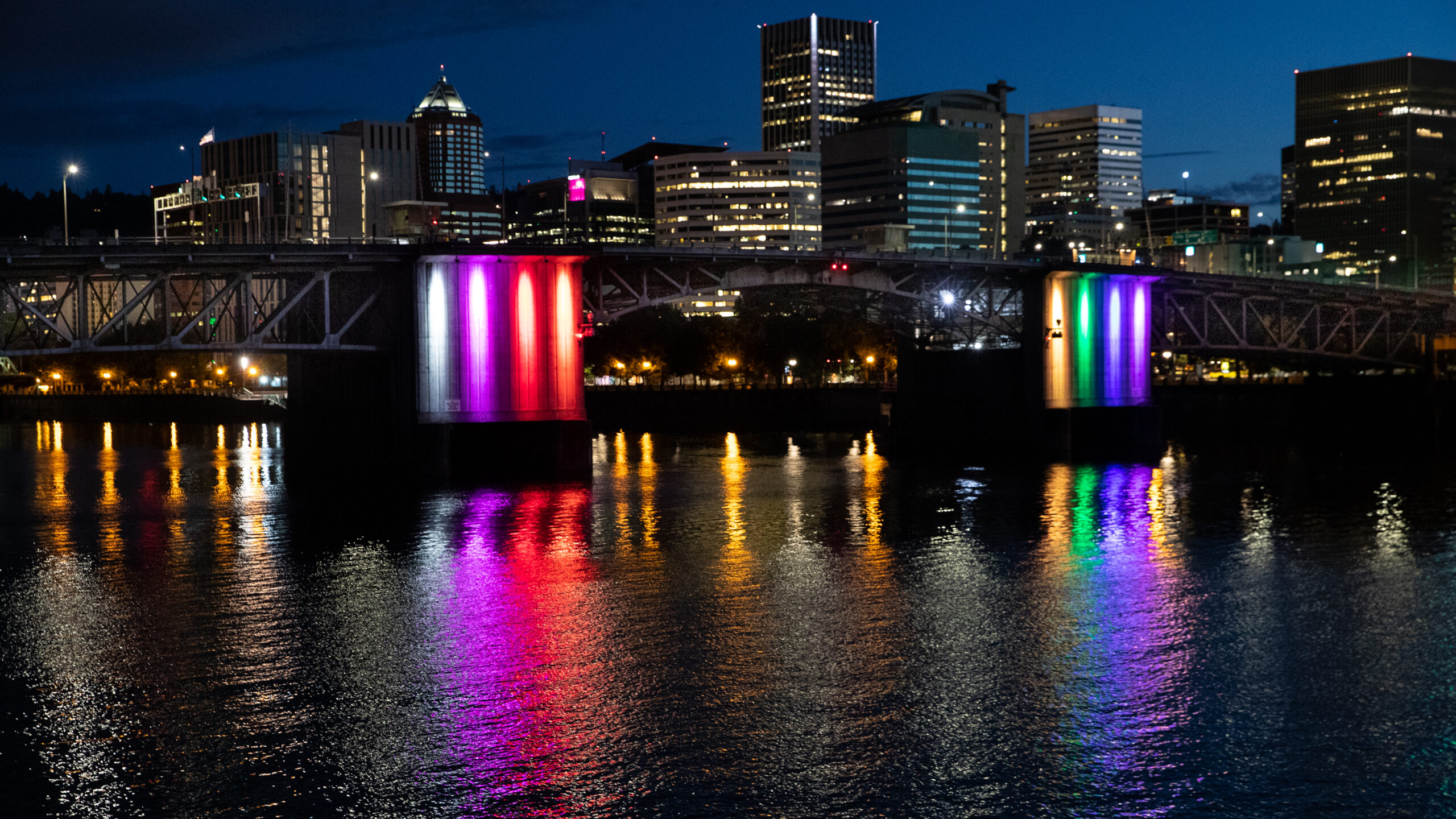 Illuminated city bridge spanning a river and city skyline at night