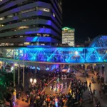 panographic shot of downtown building illuminaged at night with large crowds walking on street