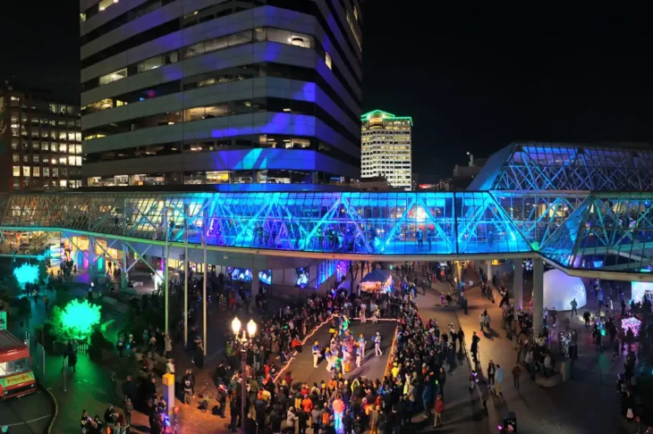panographic shot of downtown building illuminaged at night with large crowds walking on street