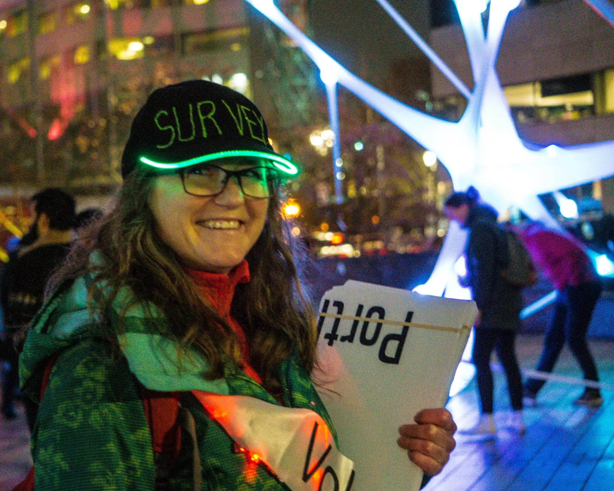 Woman outdoors winter night wearing illuminated baseball hat that says SURVEY