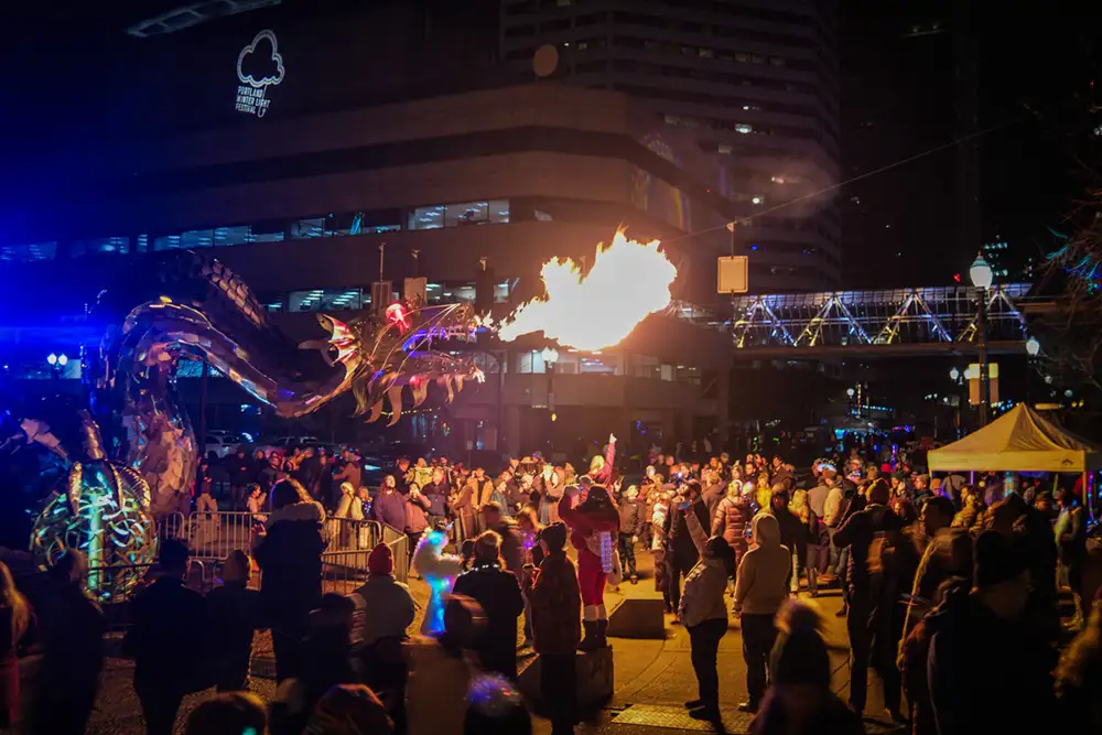 giant metal fire breathing dragon surrounded by a giant crowd at night