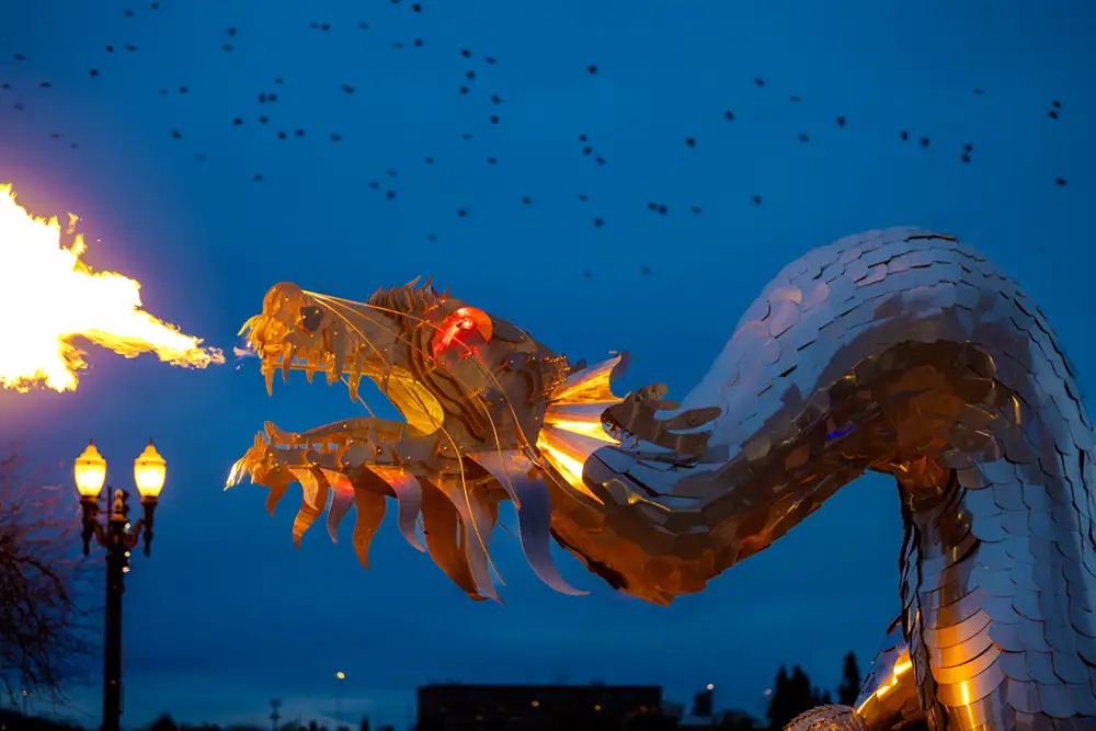 Giant metal fire-breathing dragon against a twilight blue sky with crows flying by