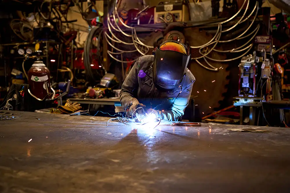 person welding wearing hood and creating bright blue sparks