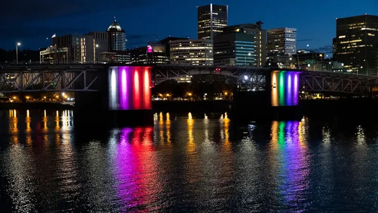 Downtown city bridge illuminated at night with rainbow colors