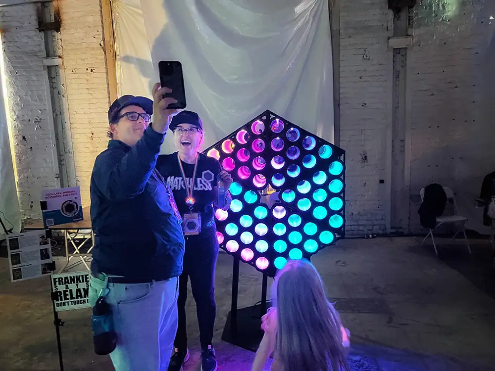 a man and a woman pose for a selfie in front of illuminated light based art scupture