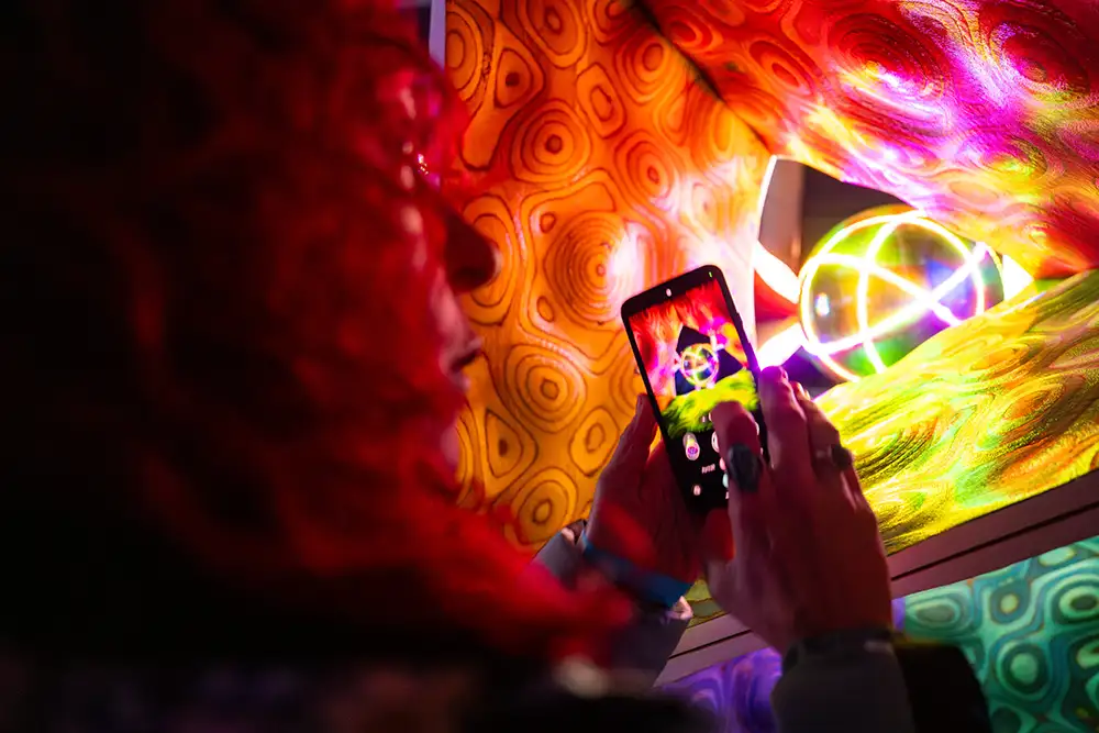 person taking phone photo of glowing pink and yellow art