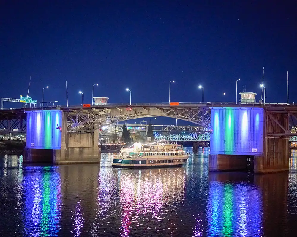 illuminated bridge at night with riverboat gliding underneath