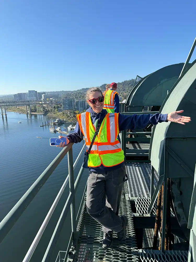 Woman wearing safety vest on top of bridge structure on a sunny day