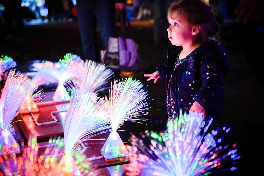 Toddler plays with glowing fiber optic light art installation outdoors at night