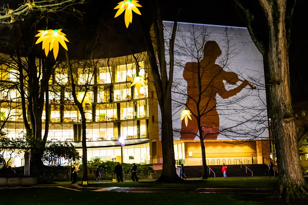 Building at night glowing with light and a projection of a violin player