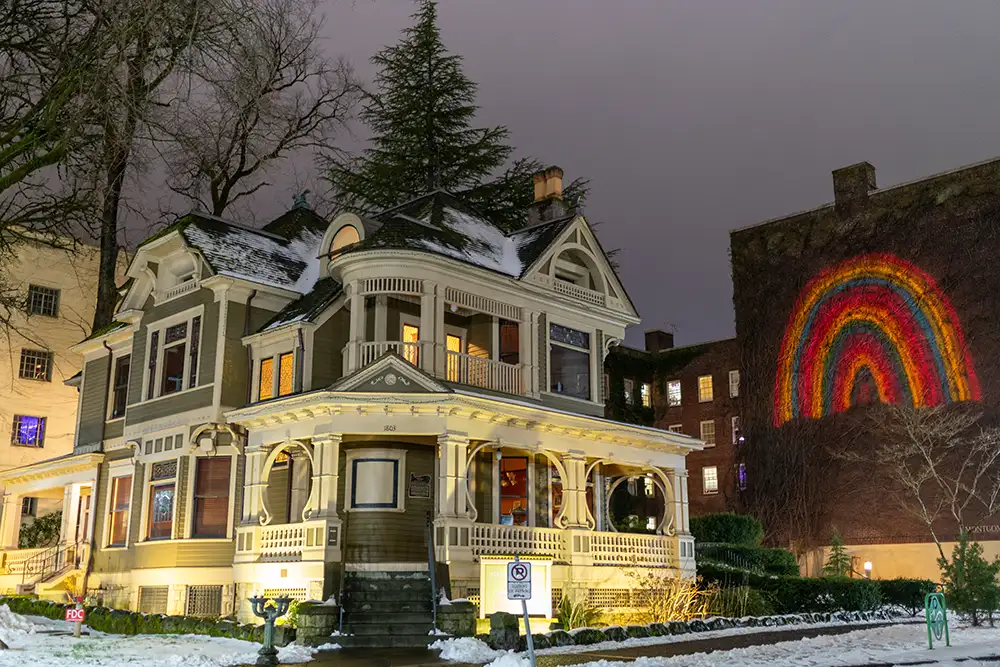 Victorian home next to building with a rainbow illustration projected onto it