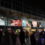 nighttime public square with screens on buildings that look like tvs