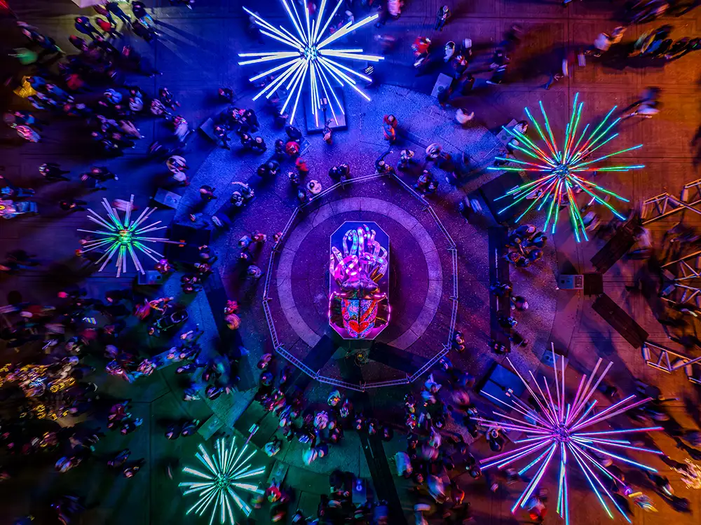drone photo of an illuminated public space at night with a crowd and 5 large art pieces